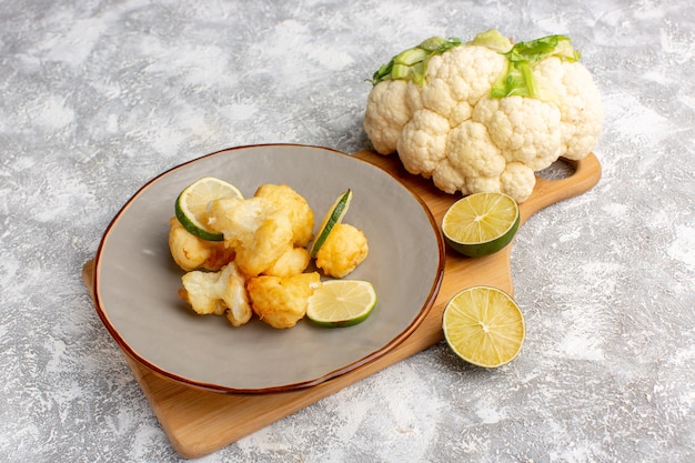 Front view of cooked sliced cauliflower inside plate with lemon on light white wall