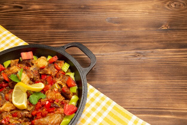 Приготовленная овощная еда с мясом и нарезанным перцем на коричневом деревянном столе, вид спереди