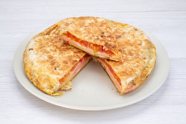 Front view of cooked vegetable pastry round inside white plate on the white surface