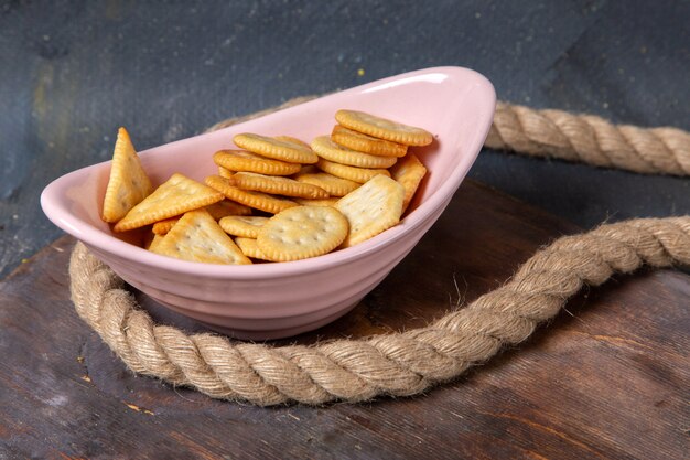 Front view of cookies and crackers inside pink plate with ropes on the wooden desk