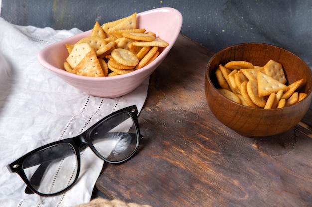 Front view of cookies and crackers inside pink plate with sunglasses on the wooden desk