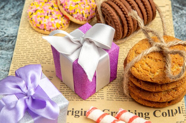 Вид спереди печенье, перевязанное веревками, рождественские подарки, красочное печенье с зефиром на газете на сером фоне