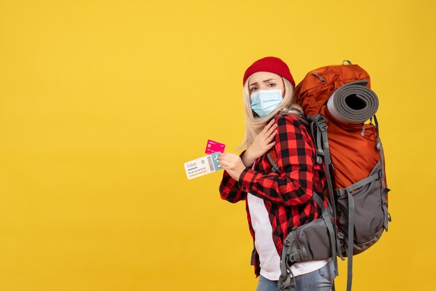 Front view cool blonde girl with her backpack holding card and travel ticket