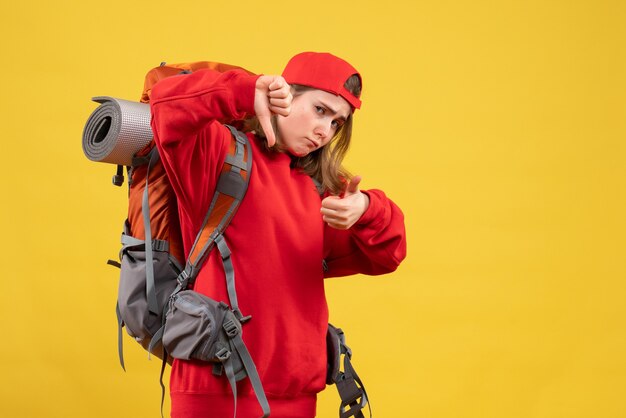 Front view cool female traveler with backpack gesturing thumbs up and down signs