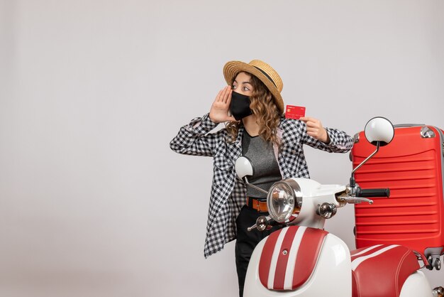 Front view of cool young girl with black mask holding ticket standing near red moped