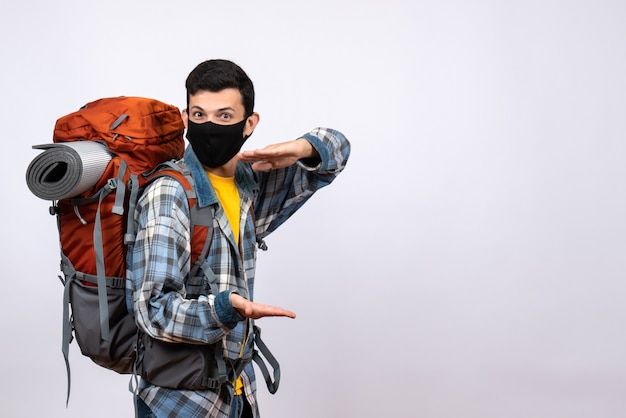 Front view cool young hiker with backpack and mask sowing size with hands