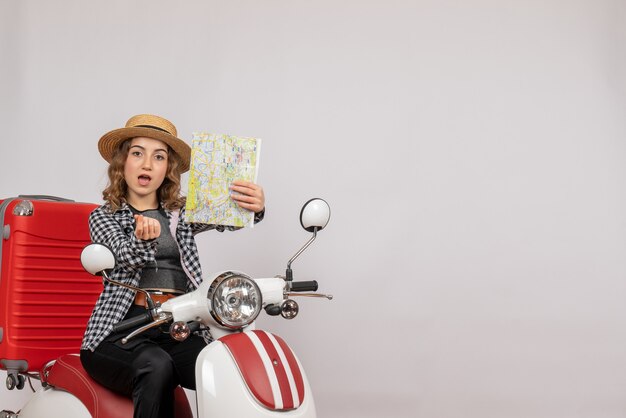 Front view of cool young woman on moped holding map on grey wall