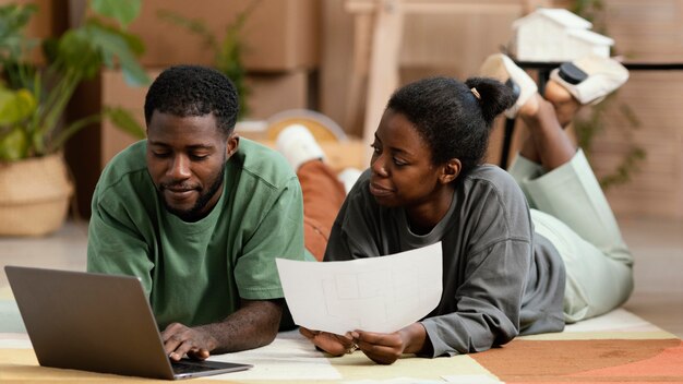 Front view of couple on the floor making plans to redecorate house with laptop