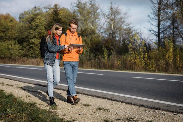 Free photo front view of couple holding map and walking along the road