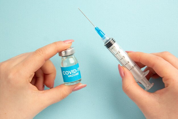 front view covid- vaccine with female trying to fill injection with it on blue background