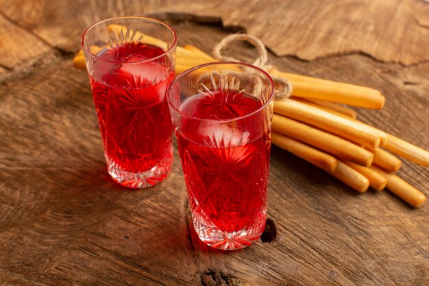 Вид спереди клюквенного сока красного цвета с палочкой крекера на деревянной поверхности