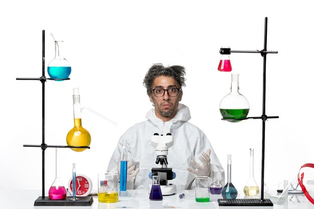 흰색 배경 실험실 질병 covid 과학 바이러스에 대한 솔루션과 함께 테이블 주위에 앉아 특수 보호 복에 전면보기 미친 남성 과학자