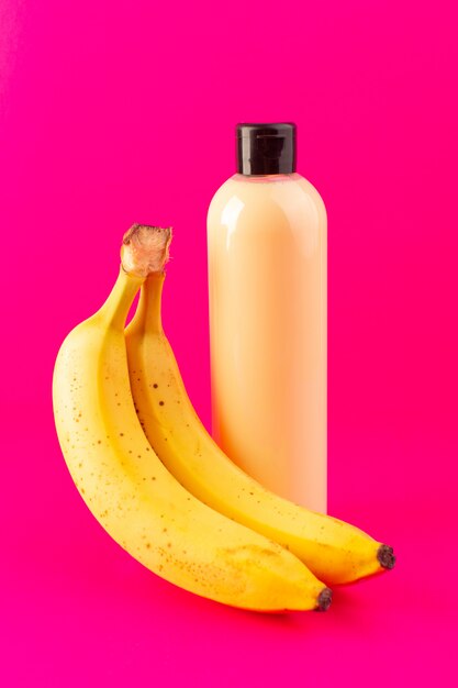 A front view cream colored bottle plastic shampoo can with black cap isolated along with bananas on the pink background cosmetics beauty hair