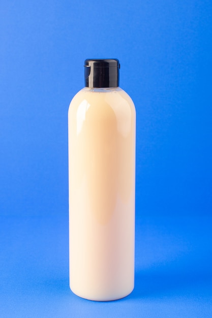 A front view cream colored bottle plastic shampoo can with black cap isolated on the blue background cosmetics beauty hair