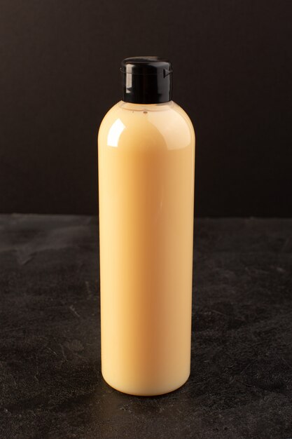 Вид спереди кремового цвета в бутылку из пластика, шампунь с черной крышкой, изолированный на темном фоне косметика для волос