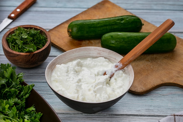 Front view of cucumbers on a board with yogurt and greens on a gray surface