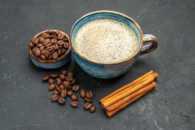 Вид спереди чашку кофе с семенами кофе и палочками корицы на темном изолированном фоне