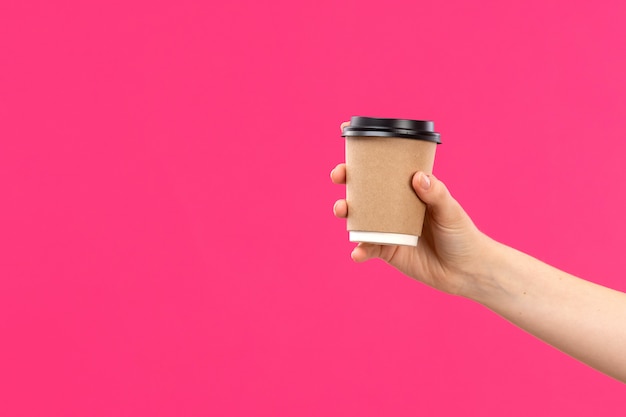 Free photo a front view cup of coffee hand holding coffee male hand pink background color drink