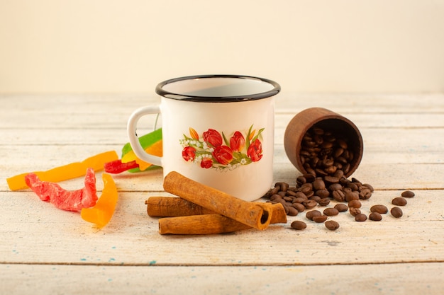 A front view cup of coffee with fresh brown coffee seeds cinnamon and colorful marmalade on the light surfacedrink coffee caffeine