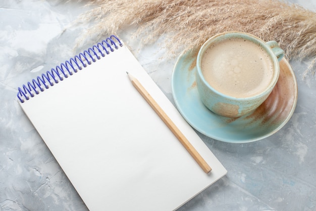 Free photo front view cup of coffee with milk inside cup along with notepad on the white desk drink coffee milk desk color