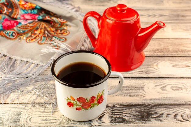 Front view of cup of coffee with red kettle on the wooden desk