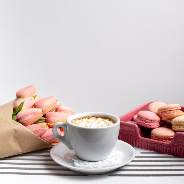 Front view of cup of marshmallows with tulips and macarons