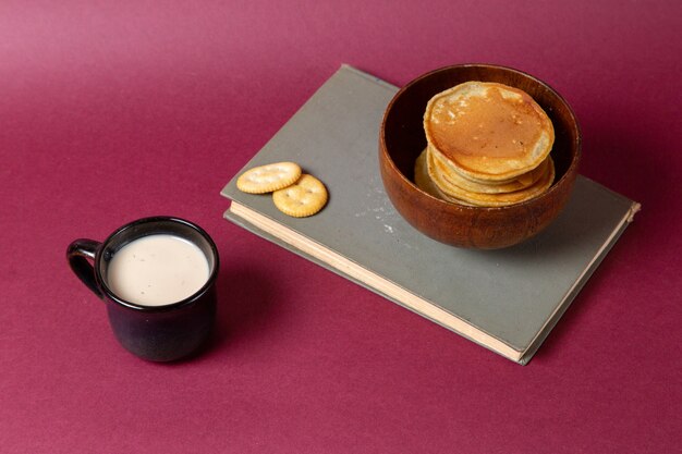 Front view of cup of milk with pancakes and crackers on the pink surface