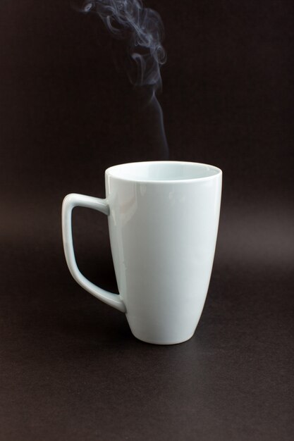 Чашка горячего чая, вид спереди, внутри белой чашки на темном столе, пить горячий чай