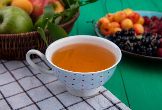 Front view of cup of tea with apples and white cherries on a green surface