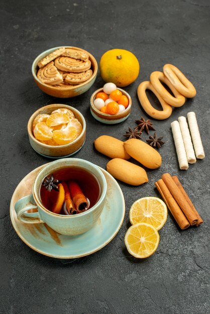 Front view cup of tea with candies biscuits and fruits on the grey table tea sweet cookie