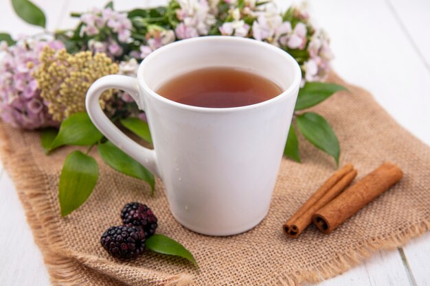 Front view of cup of tea with cinnamon and flowers on a beige napkin