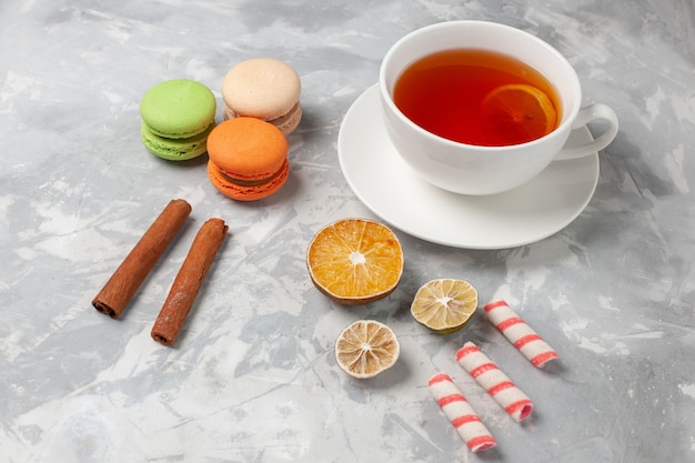 Front view cup of tea with cinnamon and french macarons on white desk