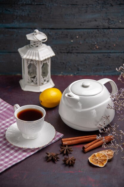 Front view cup of tea with cinnamon and kettle on dark surface tea drink lemon color