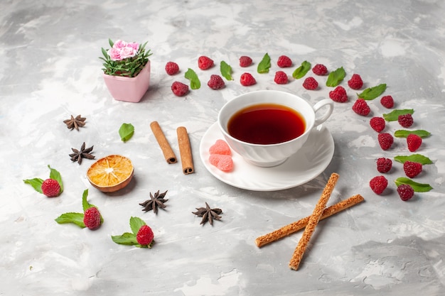 Tazza di vista frontale di tè con cannella sulla cannella della frutta della bacca del tè di superficie bianca