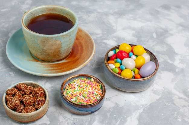 Tazza di tè vista frontale con caramelle colorate sulla scrivania bianco chiaro