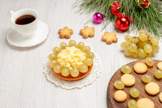 Вид спереди чашка чая со сливочным пирогом и виноградом на белом столе фруктовый чай десертный крем бисквитный торт