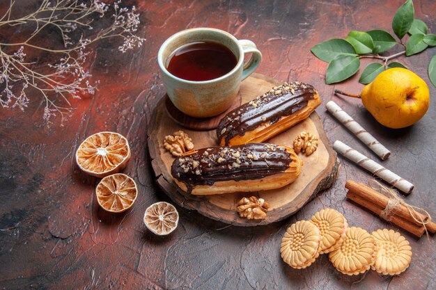 Front view cup of tea with delicious choco eclairs on dark background