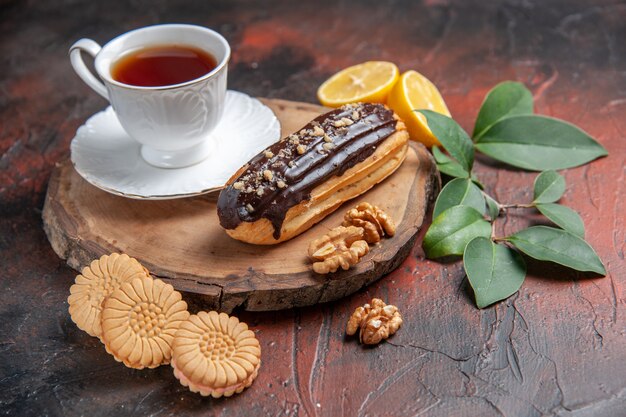 Front view cup of tea with eclair and cookies on dark background