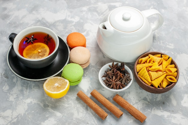 Front view cup of tea with french macarons and cinnamon on white surface