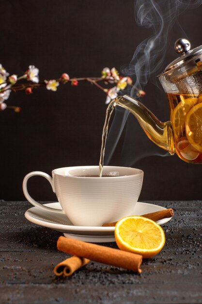 Вид спереди чашка чая с лимоном и корицей и чайник на сером столе