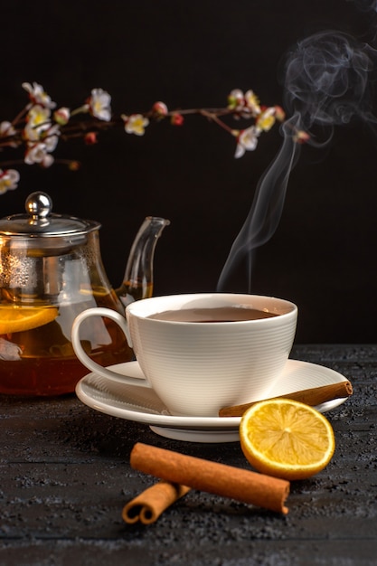 Front view cup of tea with lemon cinnamon and kettle on grey surface