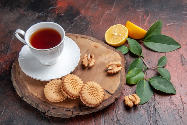 Front view cup of tea with lemon and cookies on a dark background