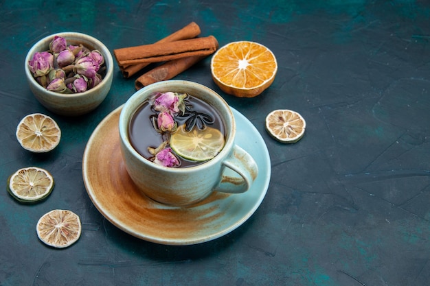 Vista frontale della tazza di tè con limone e fiori sulla scrivania scura