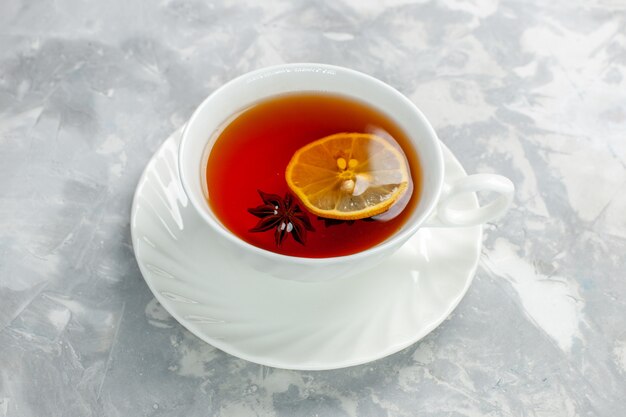 Чашка чая с лимоном на белой поверхности, вид спереди