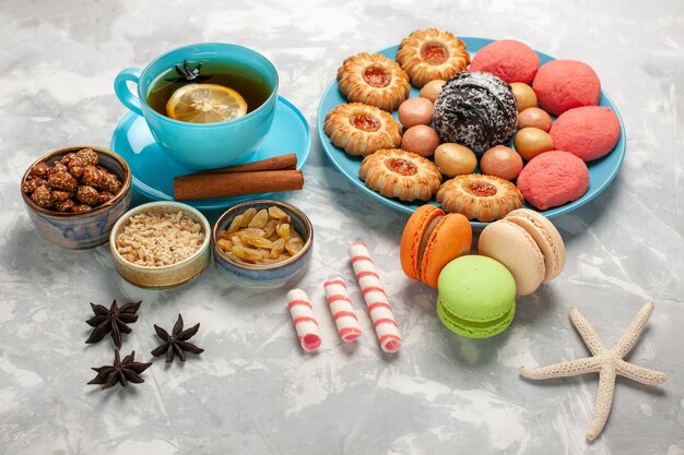 Вид спереди чашка чая с печеньем macarons и пирожными на белой поверхности, печенье, сахар, сладкий торт, конфеты