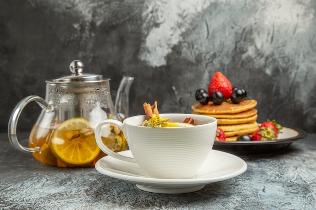 Front view cup of tea with pancakes and fruits on a dark surface morning breakfast food