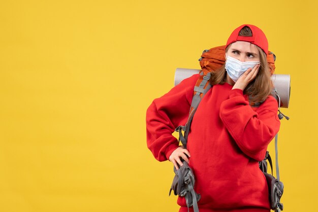 Front view curious female camper with backpack and mask putting hand on a waist and thinking