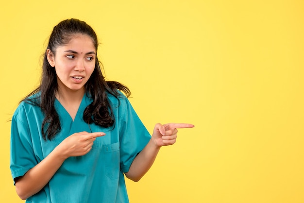 Front view curious pretty female doctor pointing at right on yellow background