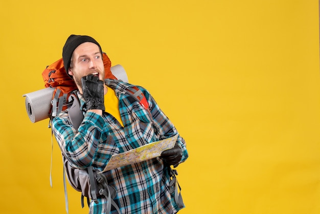 Front view of curious young backpacker with black hat holding map looking at something