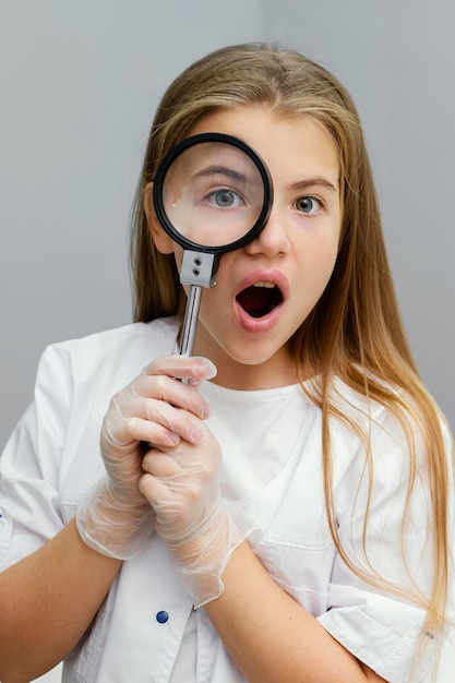 Front view of curious young girl scientist using magnifying glass